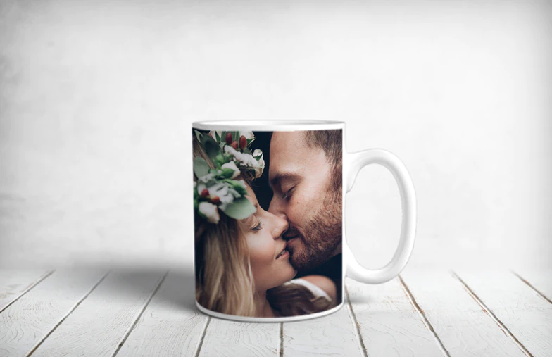 ["Personalised Photo Mugs by Printerpix", "Mother and baby holding a Printerpix mug with cartoon design and 'Dad' text", "Personalised photo mug with image of a crawling baby in an animal onesie", "Mother and daughter holding custom-designed photo mugs with family photos", "Kissing couple with personalised mugs with text on them", "Personalised photo mug with own photo of a dog on it", "", "", "", ""]